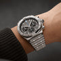 A Breitling Chronomat B01 42 stainless steel chronograph wristwatch with a black dial and three subdials featuring the Breitling 01 calibre is worn on a person’s left wrist against a neutral background.