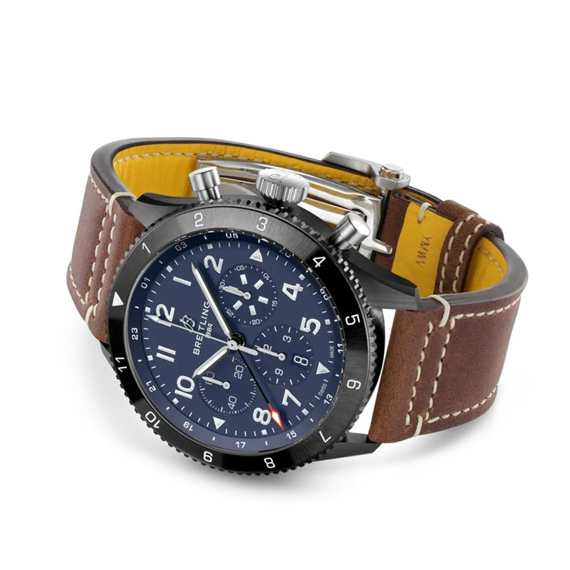 The Breitling Super AVI B04 Chronograph GMT 46 Tribute To Vought F4U features a blue dial, chronograph functions, white numerals, and a brown leather strap with white stitching—an ideal pilots watch inspired by aviation heritage.