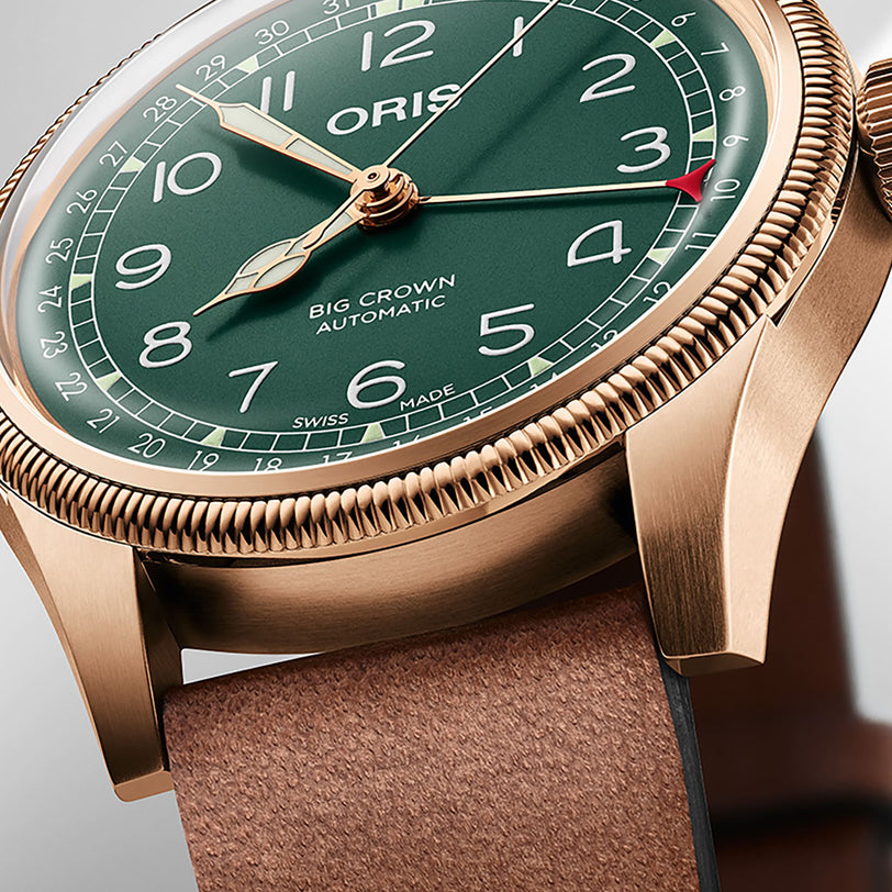 Close-up of the Oris Big Crown Pointer Date 80th Anniversary Edition, featuring a bronze case, green dial, brown leather strap, visible numerals, and displaying the time at 10:10.