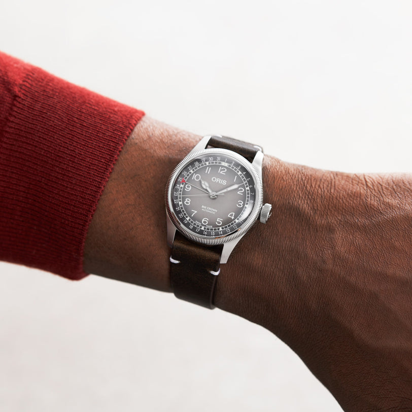 Someone wearing the striking Oris Big Crown X Cervo Volante wristwatch by Oris, featuring a brown leather strap on their left wrist against a light background—a top pick for professional pilots.