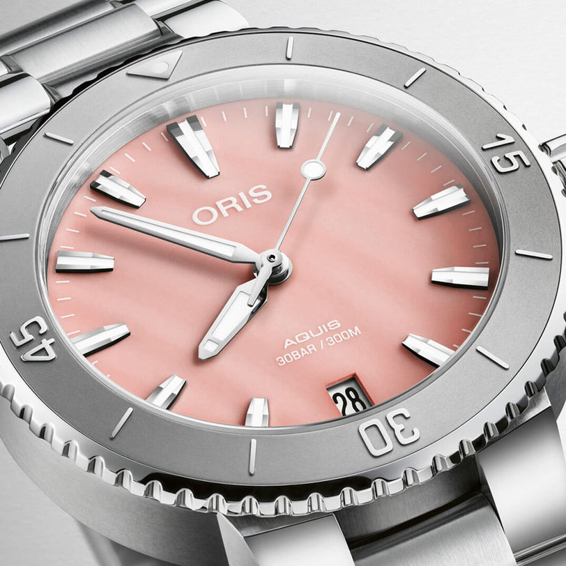 Close-up of the Oris Aquis Date watch, featuring a blush pink dial, silver hour markers, stainless steel bezel with minute markers, and a date window at 6 o’clock.