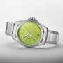 The Oris ProPilot X Kermit Edition features a stainless steel case, lime green dial, silver hour markers, date window, and metal link bracelet, showcased against a plain background and inspired by Kermit the Frog.