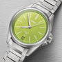 The Oris ProPilot X Kermit Edition wristwatch features a green dial, silver markers and hands, a date window at 6 o’clock, and is displayed on a textured gray surface.