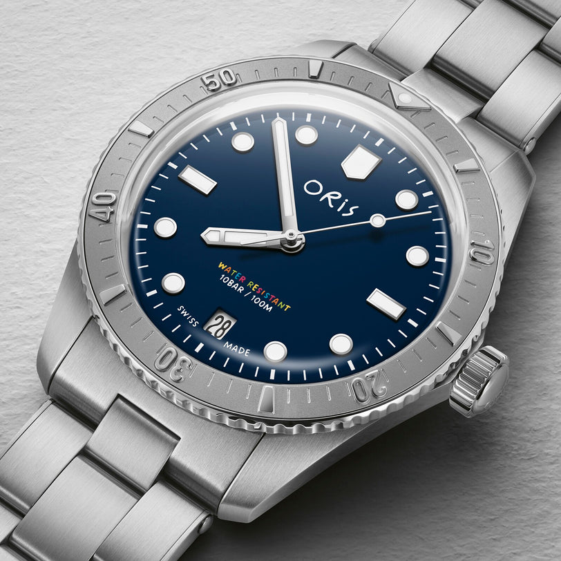 The Oris LFP Limited Edition stainless steel wristwatch features a blue dial, a date window at 6 o’clock, and a metal bracelet, showcased on a light gray textured surface.