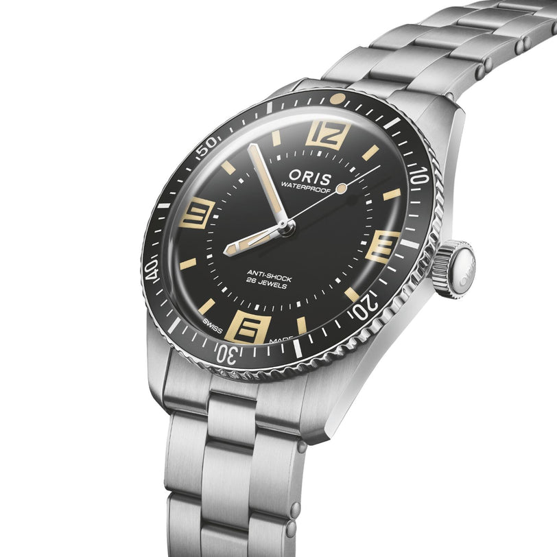 The Oris 60th Anniversary Edition dive watch, shown at an angle on a metal bracelet, features a black dial with vintage-style numerals, a rotating bezel, and a Swiss Made automatic movement for precision and reliability.