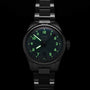 The Oris Big Crown Pointer Date Calibre 473 wristwatch with a metal band is shown in darkness, featuring glowing green numerals and hands.