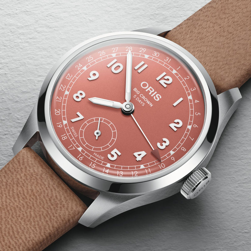 The Oris Big Crown Pointer Date Calibre 403, featuring a terracotta dial with white numerals, small seconds subdial, and tan leather strap, is displayed on a light gray textured surface.