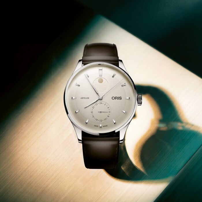 Artelier Complication watch with silver case, cream dial, moon phase subdial, and black leather strap.