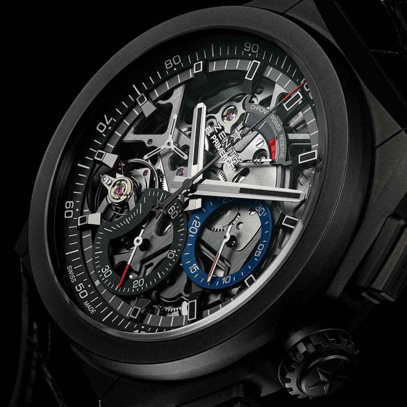 Close-up of Zenith Defy El Primero 21, a black skeleton-style wristwatch with visible gears, high-frequency chronograph subdials, and luminous hands, highlighting its intricate mechanical details.