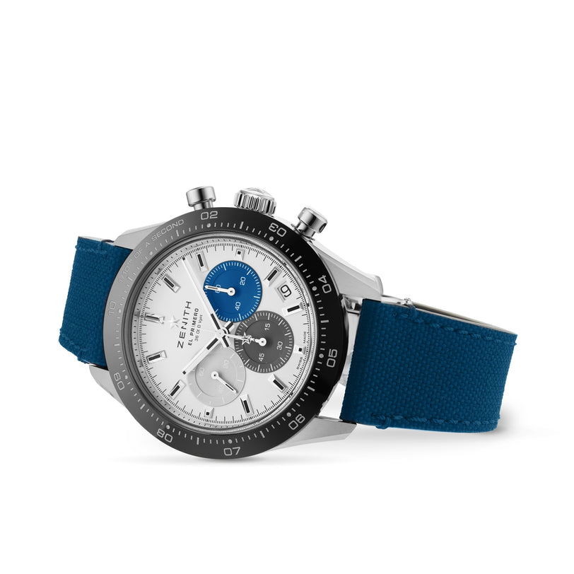 The Zenith Chronomaster Sport is a silver watch with a black bezel, blue and grey subdials, and a blue fabric strap. It features the renowned El Primero movement and is shown against a white background.
