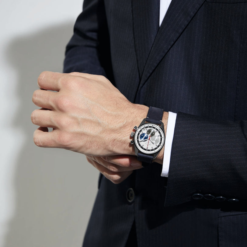 A person in a dark suit adjusts a Zenith Chronomaster EP Original wristwatch with a tricolour dial and black strap on their left wrist.
