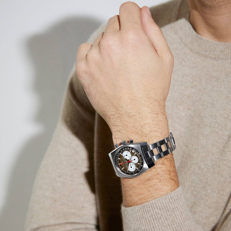A person in a beige sweater showcases a Zenith Chronomaster Revival El Primero A384 stainless steel watch with a round multi-dial face on their left wrist.