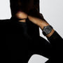 A person in a black turtleneck poses with their face mostly in shadow, showcasing the Zenith Defy Skyline, a large round black ceramic wristwatch, on their bent arm.