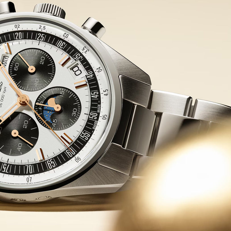 Close-up of the Zenith Chronomaster Original wristwatch with El Primero chronograph movement, three black subdials, silver and gold accents, and a metal bracelet set against a beige background.