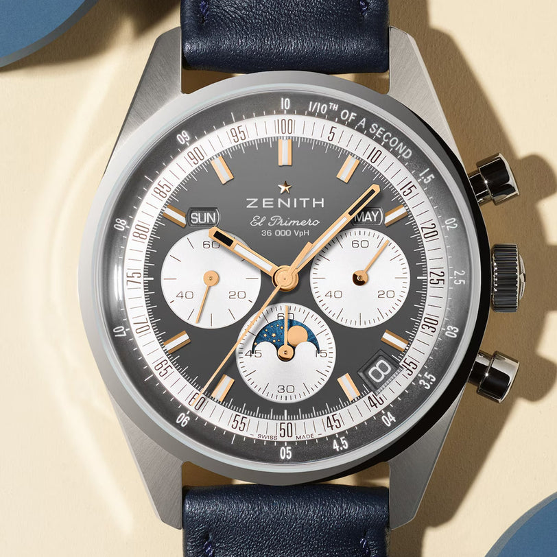 A Zenith Chronomaster Original chronograph wristwatch featuring a black dial, triple calendar, three subdials, date and day indicators, gold accents, and a blue leather strap.