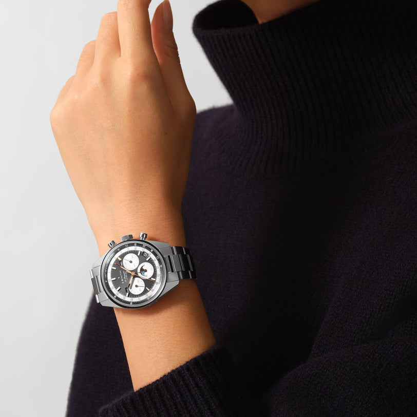 A person wears a black turtleneck and a Zenith Chronomaster Original stainless steel watch featuring three subdials, a black and white dial, and powered by the renowned El Primero 3610 movement.