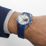 A person wears the Zenith Chronomaster Sport Centenary Exclusive with a blue bezel and strap, paired with a blue jacket and light gray cuff—an elegant selection from Watches of Switzerland.