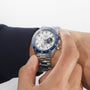 Someone adjusts the time on their left wrist, wearing a Zenith Chronomaster Sport Centenary Exclusive with a white face and blue bezel—an iconic ZENITH chronograph available at Watches of Switzerland.