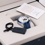 A Zenith Chronomaster Sport Centenary Exclusive wristwatch with a blue strap is displayed in an open box, accompanied by a branded tag and a card inside the lid—an elegant piece from Watches of Switzerland.