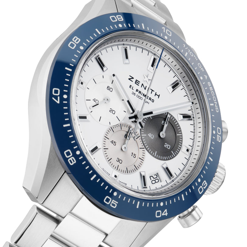 The Zenith Chronomaster Sport Centenary Exclusive features a stainless steel case, blue bezel, white dial with three subdials, and metal bracelet. Shown at an angle. Available at Watches of Switzerland.