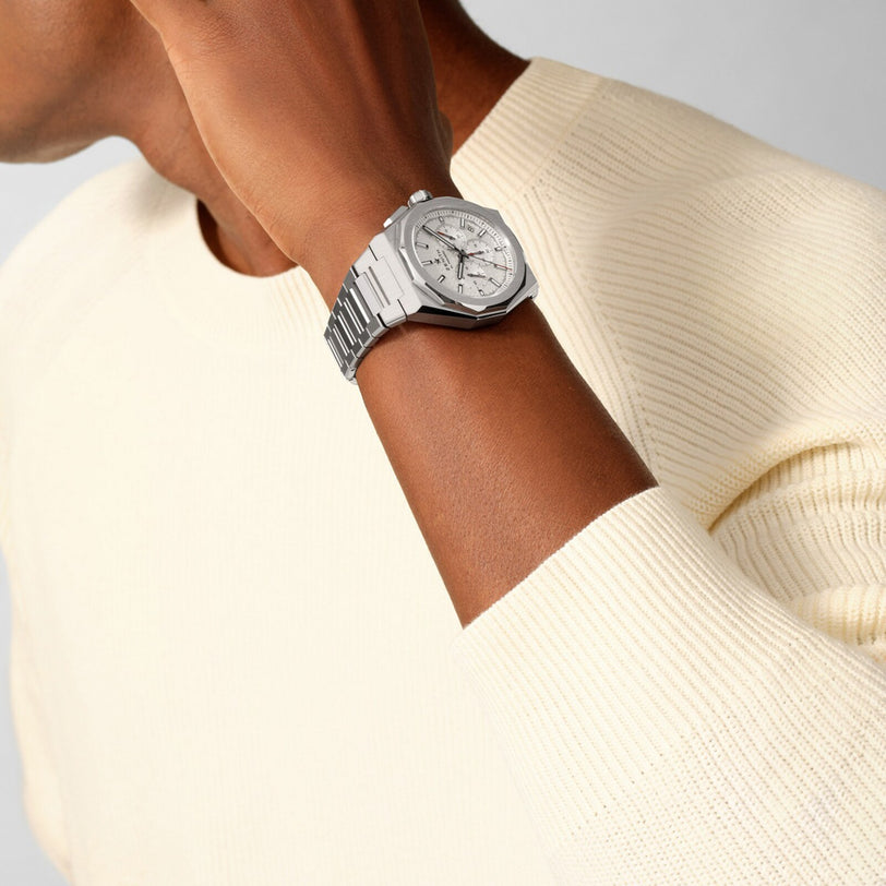A person in a cream sweater wears the Zenith Defy Skyline Chronograph, a silver wristwatch, with their hand near their ear.