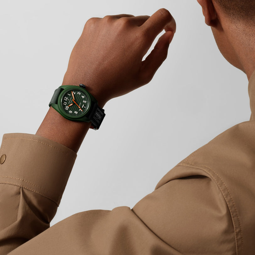 A person in a beige shirt raises their arm, displaying the Zenith Limited Edition Pilot Automatic Porter—a green watch with white numerals and a black strap.
