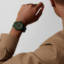 A person in a beige shirt raises their arm, displaying the Zenith Limited Edition Pilot Automatic Porter—a green watch with white numerals and a black strap.
