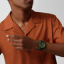 A person in an orange-brown short-sleeve shirt showcases the Zenith Limited Edition Pilot Big Date Flyback Porter with a khaki-green ceramic case on their left wrist, set against a plain background.