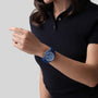 A person in a short-sleeved dark polo shirt showcases the Zenith Limited Edition Pilot Big Date Flyback 160th Anniversary Edition blue watch with an intricate face against a plain, light background.