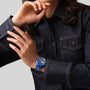 A person in a dark denim jacket wears a blue Zenith Limited Edition Chronomaster Sport 160th Anniversary Edition, featuring the El Primero 3600 mechanical design, adjusting their sleeve to highlight its high-frequency timekeeping.