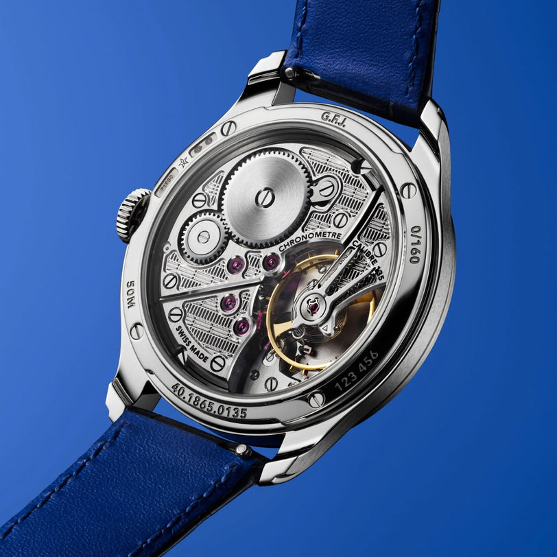 Close-up of the Zenith Limited Edition G.F.J. Calibre 135 160th Anniversary watch’s open case back, revealing its detailed mechanical movement in a platinum round case with a blue leather strap, set against a blue background.