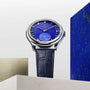 The Zenith Limited Edition G.F.J. Calibre 135 160th Anniversary wristwatch with a blue dial and leather strap is shown upright among geometric stone-like blocks, highlighting its platinum round case.