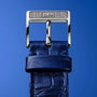Close-up of a shiny silver G.F.J. buckle on a textured blue leather strap from Zenith’s Limited Edition G.F.J. Calibre 135 160th Anniversary Edition, set against a solid blue background.