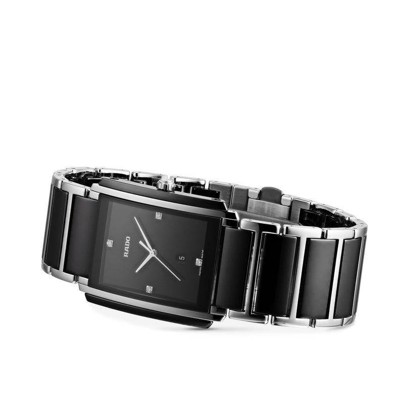A black and silver rectangular Rado Integral Diamonds watch with a metal link band, black face, silver markers, and precise quartz movement is displayed on a white background.