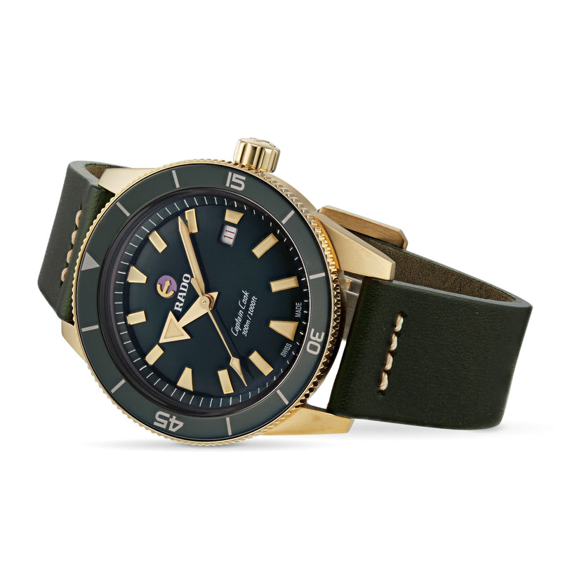 The Rado Captain Cook Automatic Bronze displays a gold-tone bronze case, black dial with date, rotating bezel, and dark green leather strap—all shown at an angle.