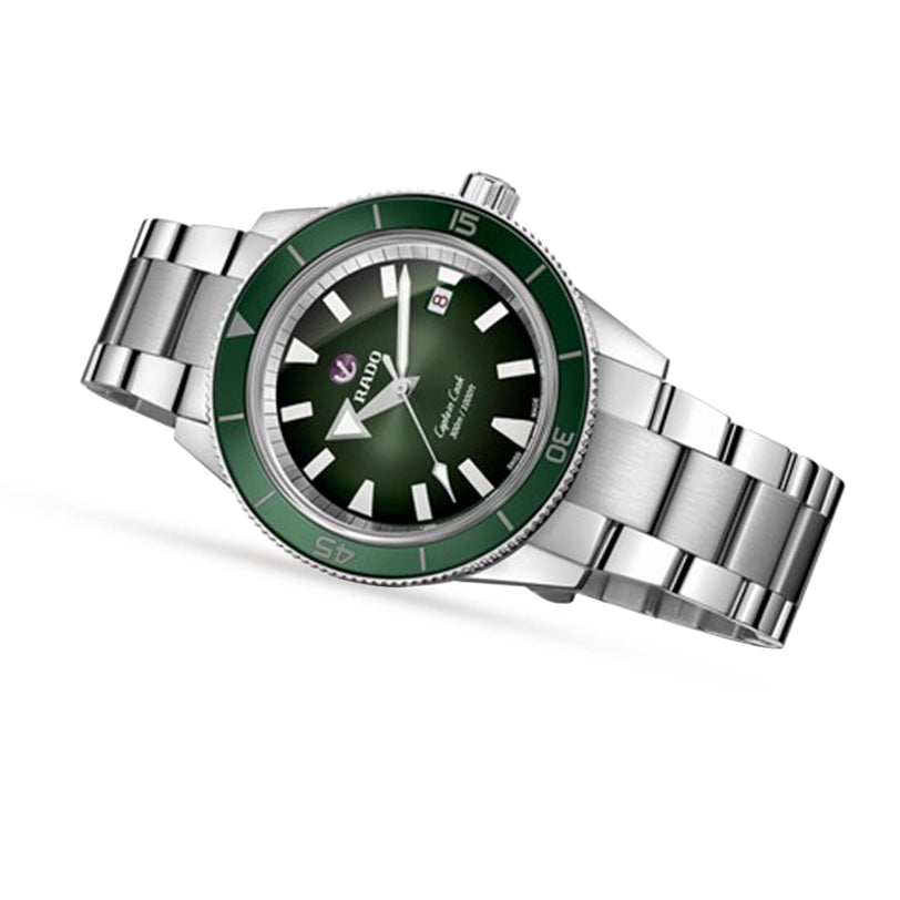 The Rado Captain Cook Automatic is a silver stainless steel wristwatch featuring a green bezel and dial, white hour markers, vintage-inspired details, and a date window at 3 o’clock.
