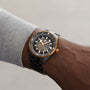 A person wearing a Rado Captain Cook High-Tech Ceramic wristwatch in black and gold, featuring a partially transparent dial that reveals the internal gears, set against a plain background.