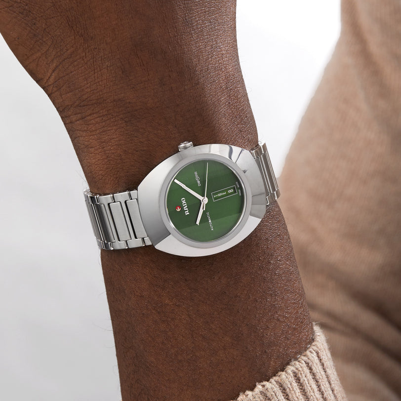 Someone wearing the Rado DiaStar Original on their left wrist—a silver watch with a green dial, sapphire crystal, date display, automatic movement, and metal band.