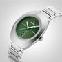 A silver metal wristwatch from Rado DiaStar Original, with a green oval face, sapphire crystal, automatic movement, and date-day display on a light gray background.