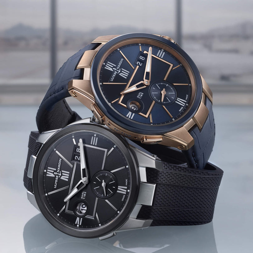 Two luxurious Ulysse Nardin Blast Dual Time watches—one in rose gold and blue, the other in silver and black—feature Roman numeral dials, Dual Time and Home Time functions, set against a softly blurred background.
