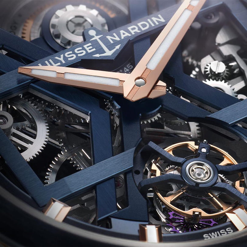 Close-up of the Ulysse Nardin Blast Tourbillon watch face, highlighting blue and rose gold hands, visible gears, and detailed mechanical components that exemplify haute horology.