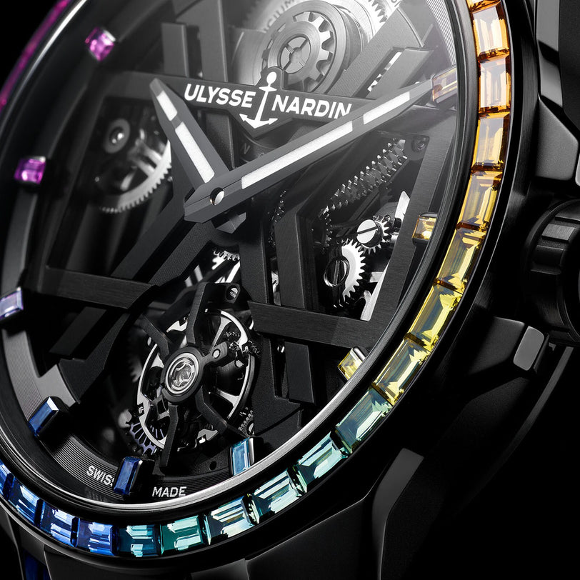 Close-up of the Ulysse Nardin Blast Tourbillon Rainbow watch, highlighting its black skeleton X dial, bezel adorned with multicolored gemstones, and intricately visible gears.