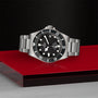 The TUDOR Pelagos, a stainless steel divers tool watch with a black dial and rotating bezel, is displayed on a red platform against a textured black background.
