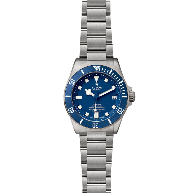 The TUDOR Pelagos is a stainless steel diving watch featuring a blue bezel and dial, white hour markers, Swiss Chronometer precision, date display at 3 oclock, and a metal bracelet.