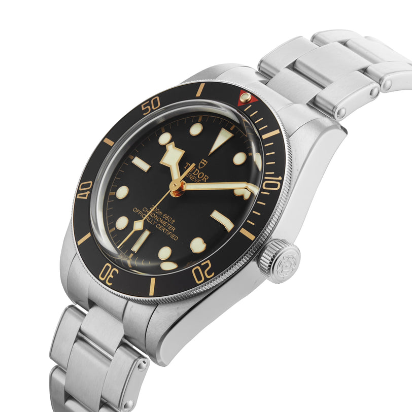 The TUDOR Black Bay 58 is a stainless steel wristwatch featuring a black bezel, black dial, large luminescent markers, a steel bracelet, and orange accents on the hands and bezel—evoking classic vintage-inspired diver style.