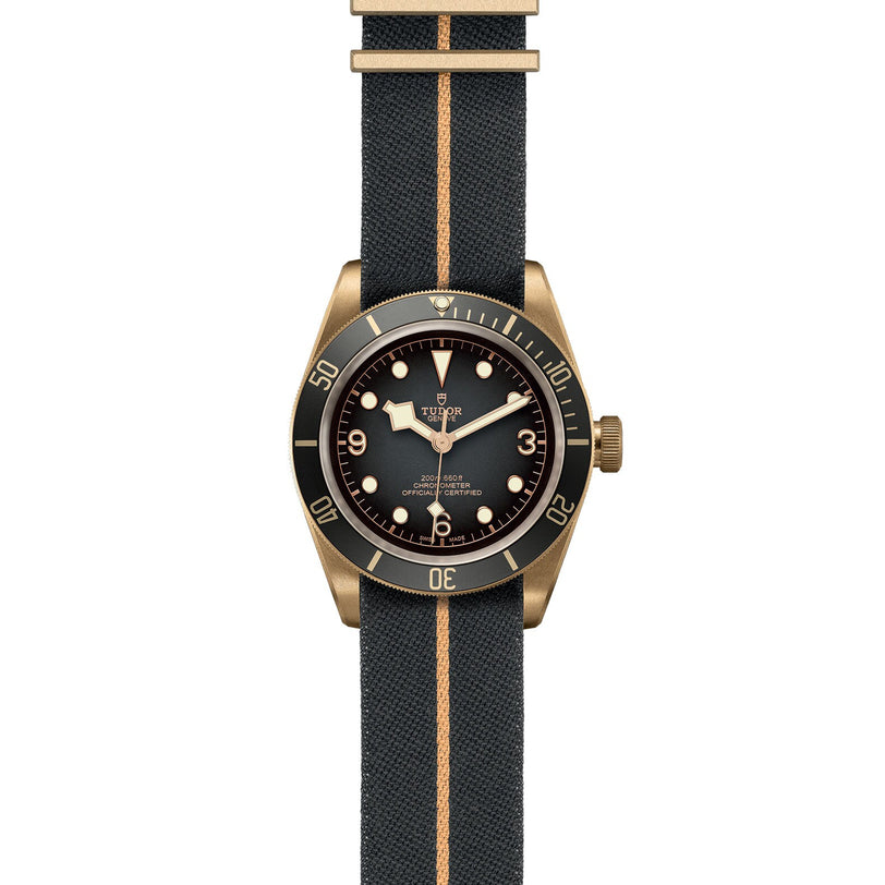The TUDOR Black Bay Bronze is a diving watch with a dark dial, gold accents, and a fabric strap featuring a matching center stripe—blending premium craftsmanship with timeless style.