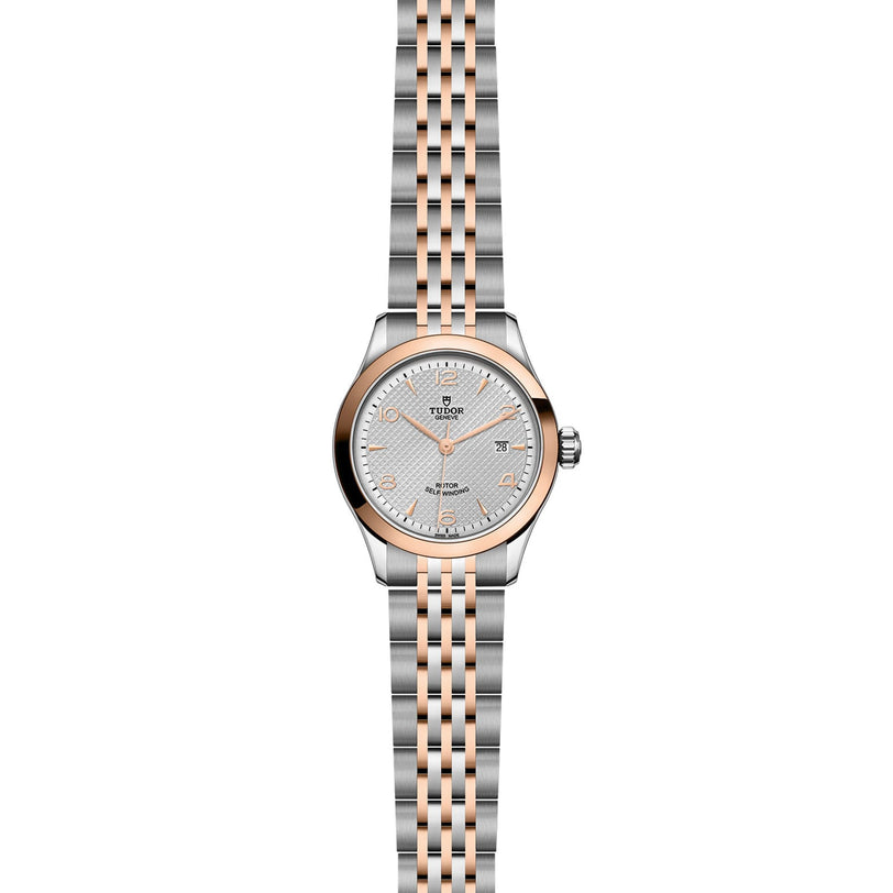 The TUDOR 1926 is a silver and rose gold wristwatch featuring a patterned white dial and a linked metal bracelet.