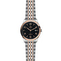 The TUDOR 1926 wristwatch features a round black dial, gold-tone markers and hands, a date display, and a two-tone silver and rose gold bracelet—an elegant nod to TUDOR’s tradition in fine mechanical watches.