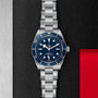 The TUDOR Black Bay 58, featuring a stainless steel case with a blue dial and bezel, is displayed on a textured black surface with silver and red accents—an iconic modern divers watch.