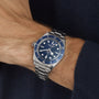 A TUDOR Black Bay 58 watch with a blue bezel and dial is worn on a wrist, paired with a dark long-sleeve garment.
